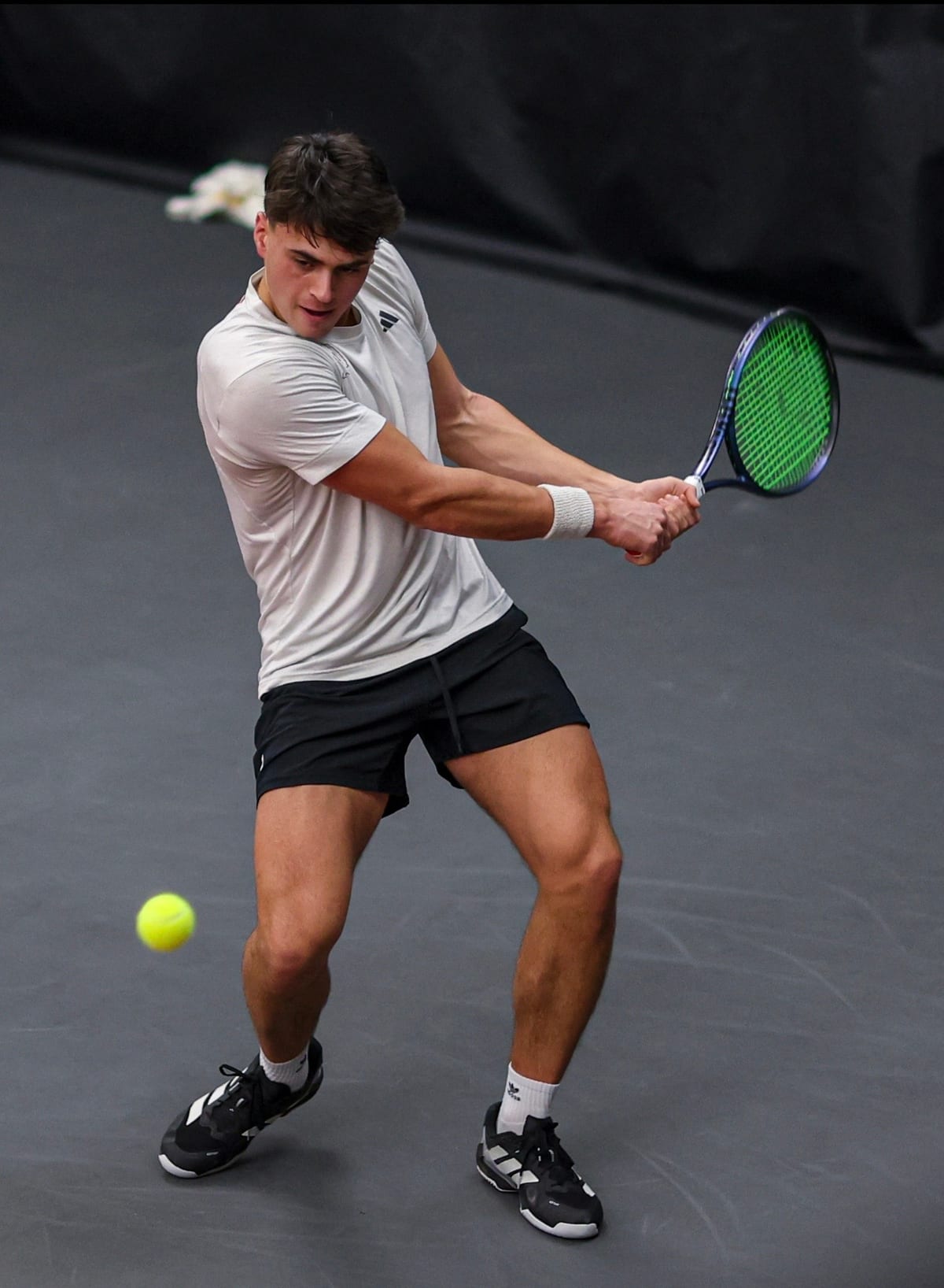 A coach driving through a two-handed backhand on an indoor court